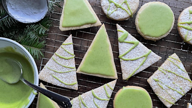 Green-iced tree, circle, and square Christmas cookies on cooling rack with bowl