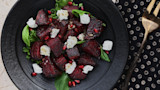Roasted beet salad with goat cheese, pomegranate seeds and greens on black plate