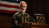 Judge in camouflage robe at bench with American flag behind