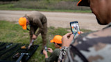 Hunter photographing two hunters in orange caps field-dressing a bird by pickup truck bed