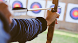 Archer drawing a wooden bow with nocked arrow, aiming at multicolored bullseye targets
