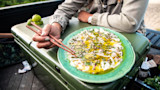 Person using wooden chopsticks labeled 'KEEP WILD' to pick fish carpaccio with capers on green plate