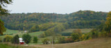 Rural autumn valley with rolling wooded hills, fields, red barn and farmhouse