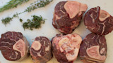 Raw cross-cut shanks with exposed marrow and rosemary and thyme on a white cutting board