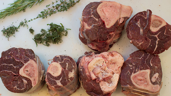 Raw cross-cut shanks with exposed marrow and rosemary and thyme on a white cutting board