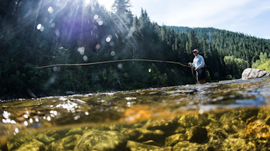 Angler casting fly rod in a mountain river, underwater rocks visible