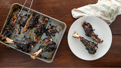 Korean BBQ charred turkey wings on baking sheet and two on white plate with scallions and chili flakes