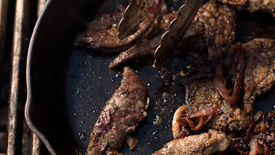 Wild-game liver and caramelized onions sizzling in cast-iron skillet with tongs