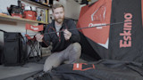 Man kneeling holding an ice-fishing pole beside an Eskimo Outbreak 450i shelter
