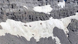 Rocky mountain cliff and snowfield with multiple small dark spots circled on the snow