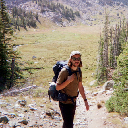 Hiker with backpack and sunglasses on mountain meadow trail