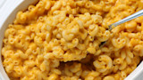 Butternut squash mac and cheese in white bowl, spoon lifting cheesy cavatappi pasta