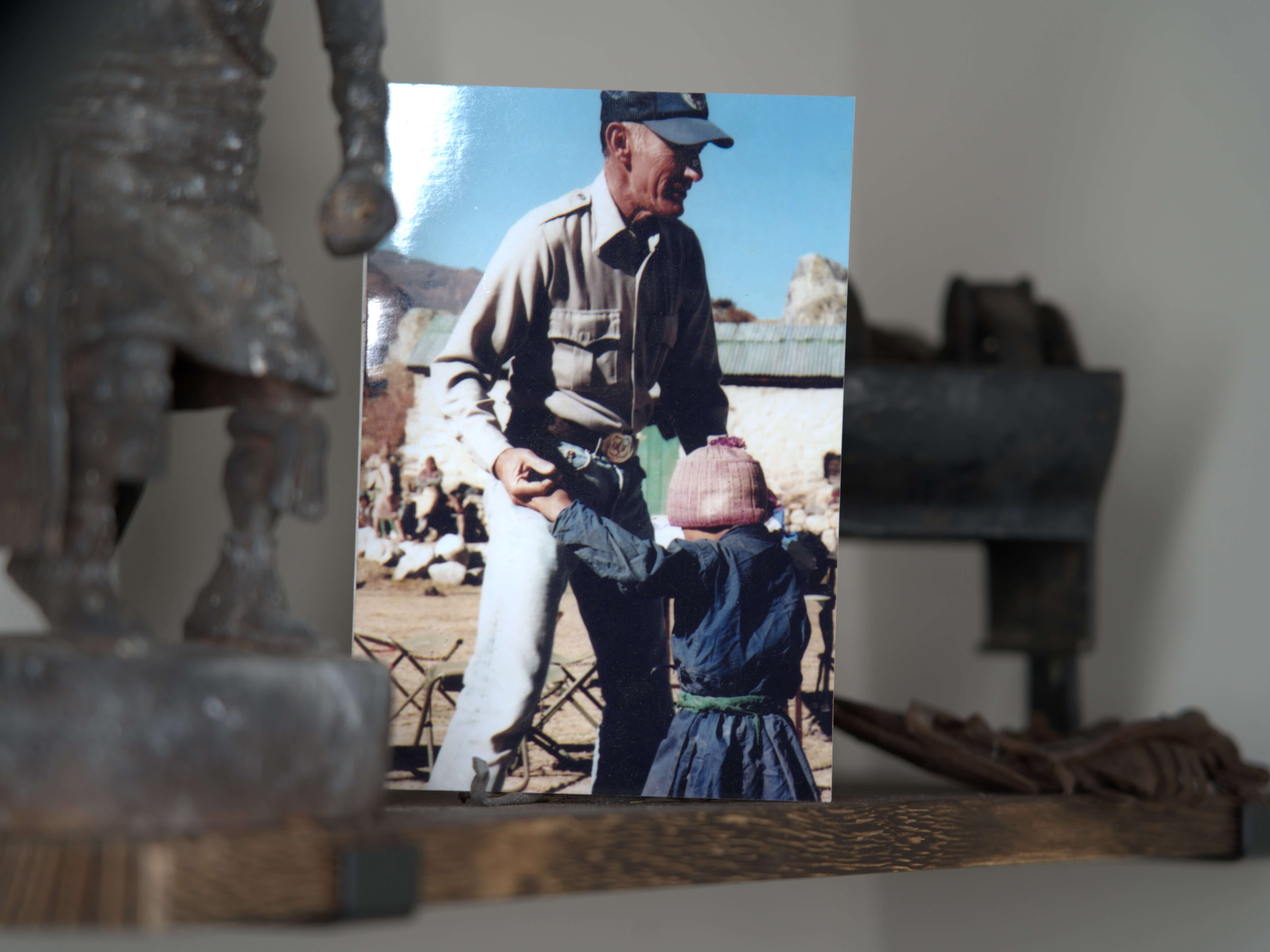 Printed photograph of a man in a cap holding a child in a pink knit hat outdoors, propped on a shelf