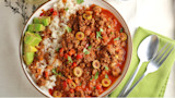 Venison picadillo with rice, sliced avocado, green olives and cilantro in bowl; spoon and fork on green napkin
