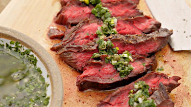 Sliced medium-rare skirt steak with chimichurri on wooden cutting board