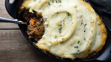 Cast-iron shepherd's pie topped with mashed potatoes and herbs, spoon revealing venison filling