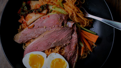 Sliced duck breast on noodles with soft‑boiled egg, kimchi, cucumber, carrots and sesame