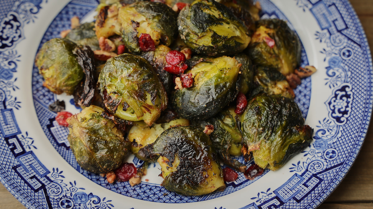 Smashed roasted Brussels sprouts with dried cranberries and chopped walnuts on blue plate