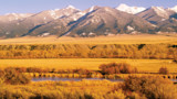 Autumn river valley with a small pond, golden grasses, and snow-capped mountains