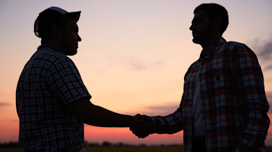 Two men silhouetted shaking hands against a sunset sky