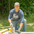 Man kneeling cutting lumber with a circular saw, wearing blue shirt with white antler logo