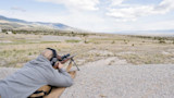 Man lying prone firing a scoped rifle on a bipod at distant targets on an open shooting range