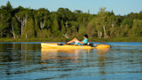 Man fishing from yellow kayak on calm lake with tree-lined shore