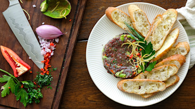 Duck tartare with crostini, lemon zest and parsley; cutting board with knife, shallot, avocado.