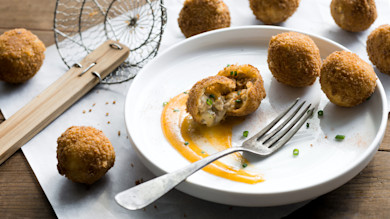 Fried venison-sausage pimento-cheese croquettes, one split on plate with sauce smear, fork