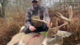 Hunter kneeling behind harvested buck with large antlers and blood on its side