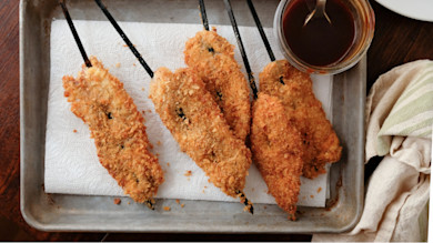 Breaded turkey katsu skewers on a baking tray with a jar of dipping sauce