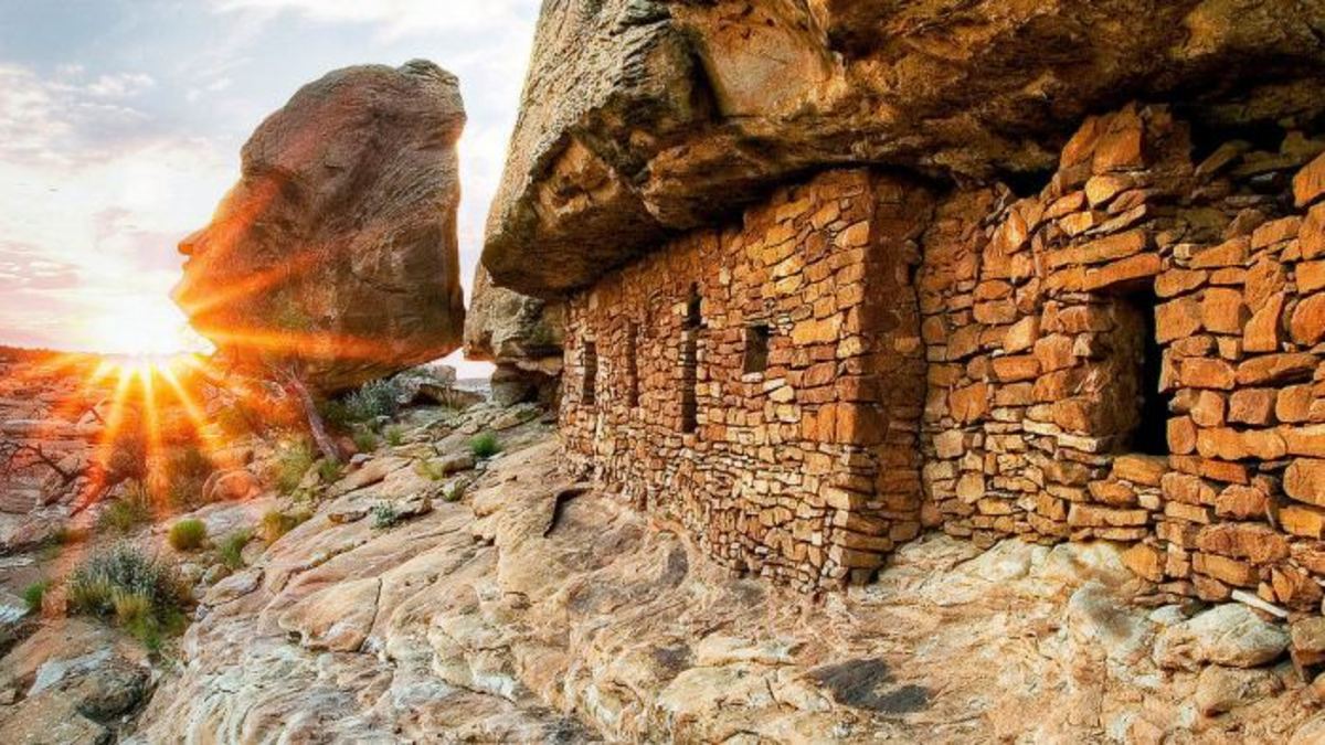 Ancestral Pueblo cliff dwellings in a sandstone overhang with sunburst on the horizon at sunset