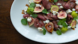 Grilled sliced goose with halved figs, goat cheese, mint leaves and balsamic on white platter