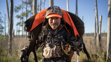Hunter carrying moose over his shoulders wearing camouflage and an orange cap