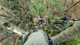 Treetop view down at hunter in camouflage holding binoculars on laddered tree stand with compound bow