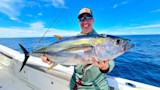 Man holding large yellowfin tuna on a boat in open blue ocean