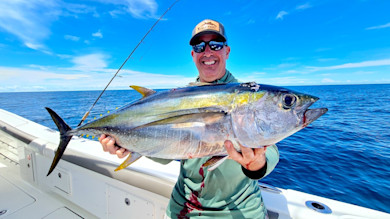 Man holding large yellowfin tuna on a boat in open blue ocean
