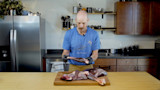 Man in blue MEATEATER shirt removing venison shank on cutting board