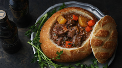 Beef and vegetable Guinness stew in hollowed bread bowl with parsley and Guinness bottles