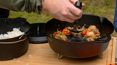 Fish fillets being ladled from a cast-iron pot; rice in pot beside, garnished with sliced red chili and scallions
