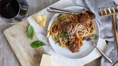 Spaghetti with meatballs in tomato sauce, fresh basil and grated cheese on a white plate