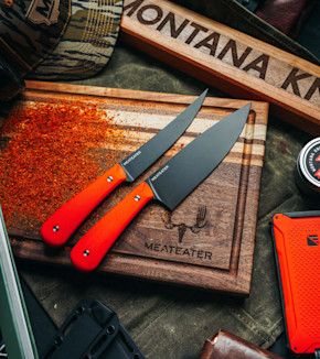 Two orange-handled knives on engraved wooden cutting board reading MEATEATER