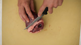 Hands slicing a game heart with a knife on a yellow cutting board