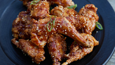 Crispy Korean-style fried rabbit pieces glazed with sesame and scallions on black plate