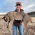 Woman holding a dead bobcat across her arms, smiling in a grassy field