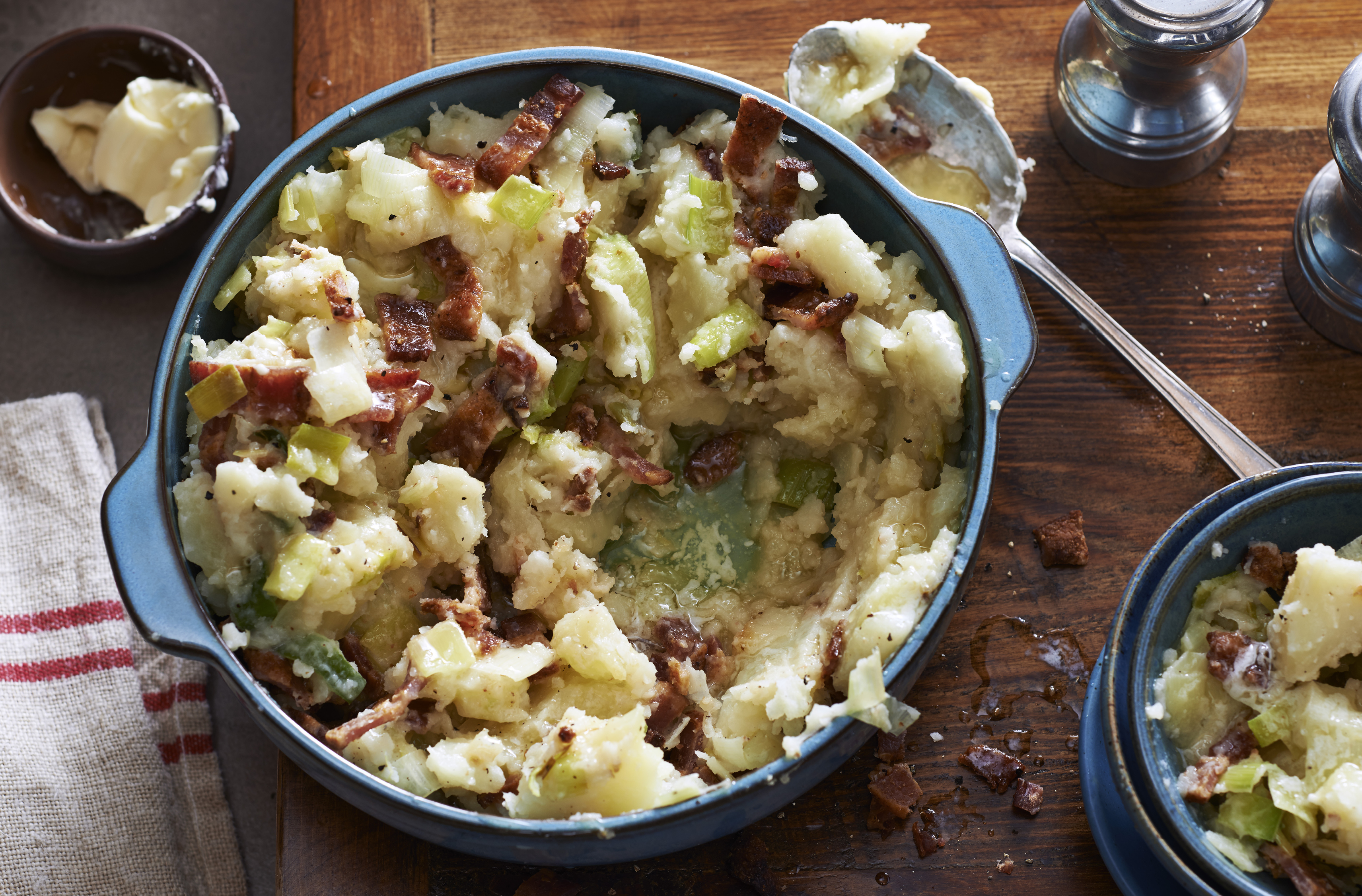 Mashed potatoes recipe mixed with leek and bacon.  Placed in a ceramic serving bowl.  Small butter dish on the side to place on top.