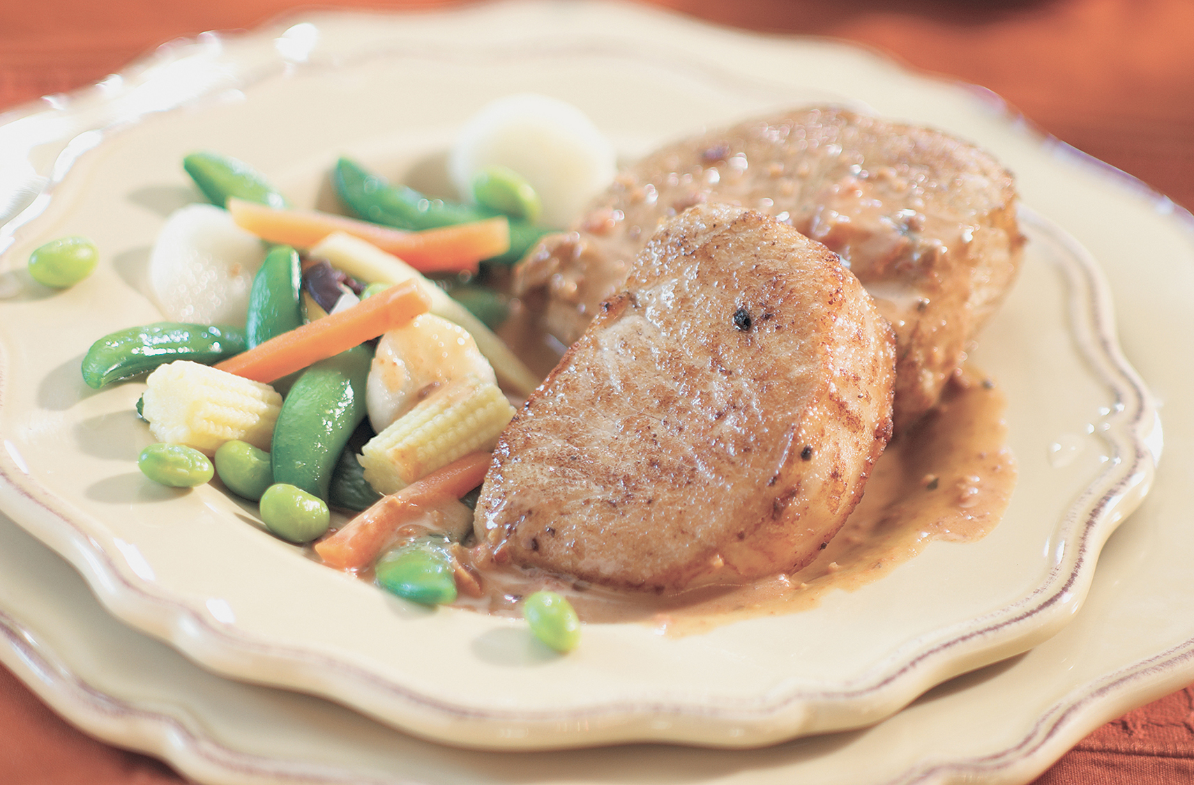 two pieces of saucy szechwan pork chops served on a cream coloured plate with steam mixed vegetables on the side