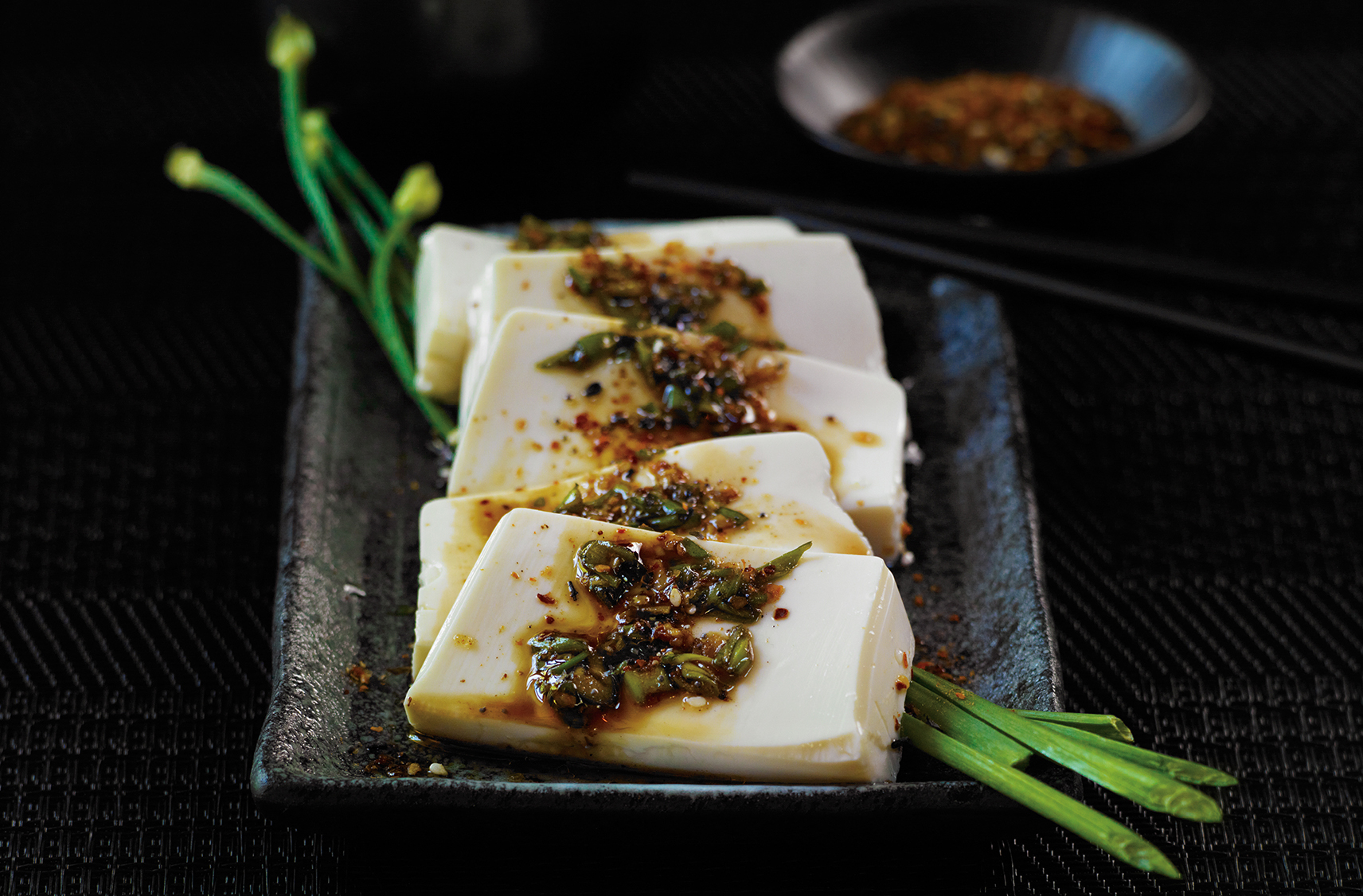 5 slices of tofu on a platter, garnished with Asian sauce & togarashi spice