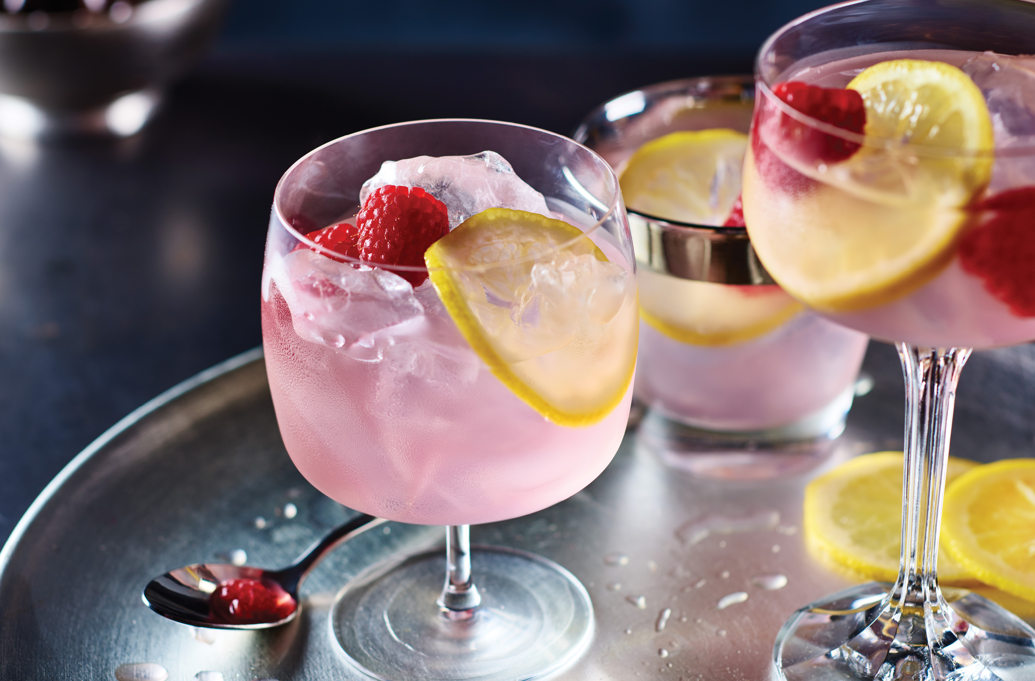3 glasses of pink ginger kicker cocktail with raspberries and lemon slices as garnish
