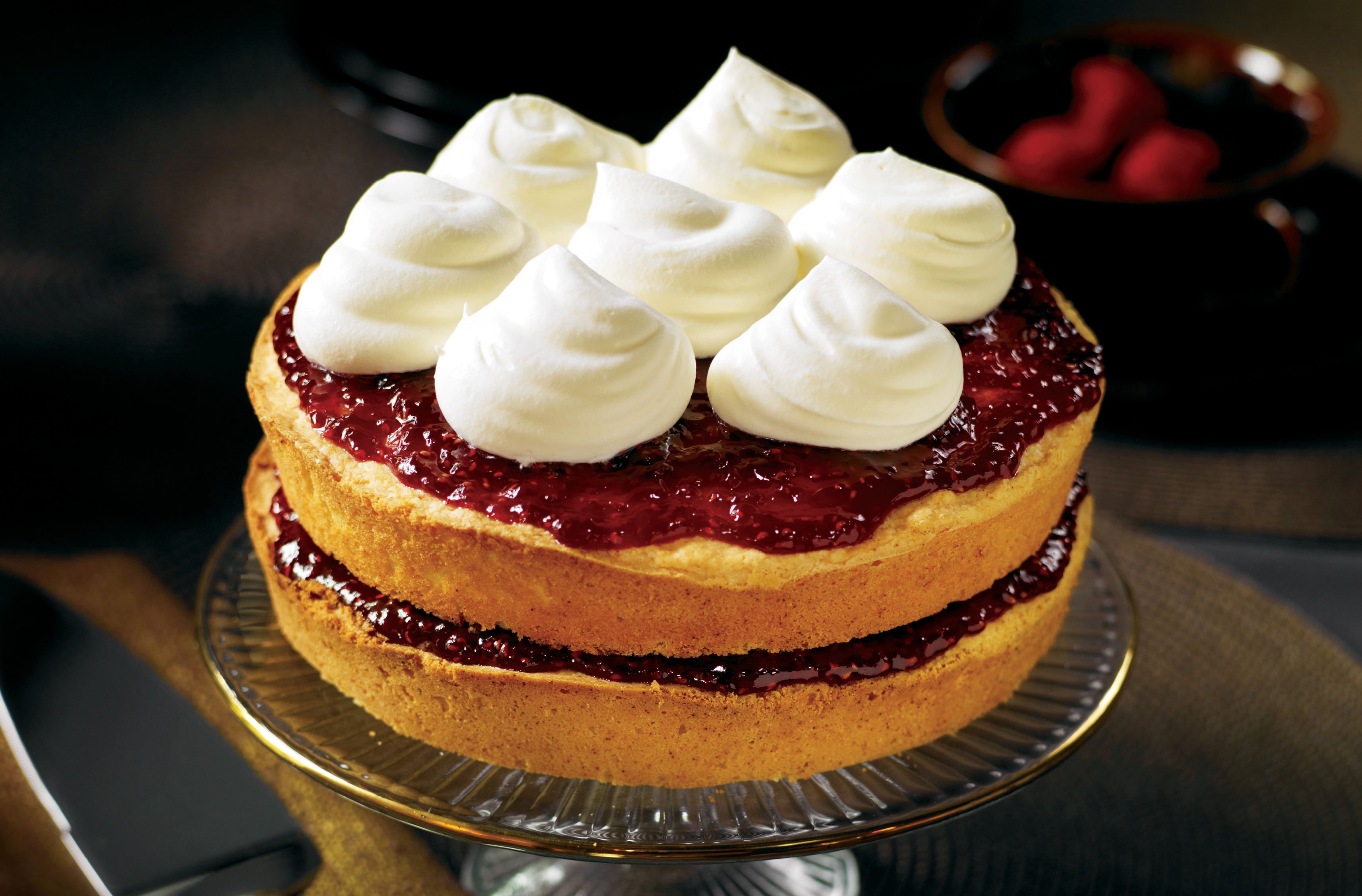 A 2 layer cake, filled & topped with raspberry fruit spread & whipped cream
